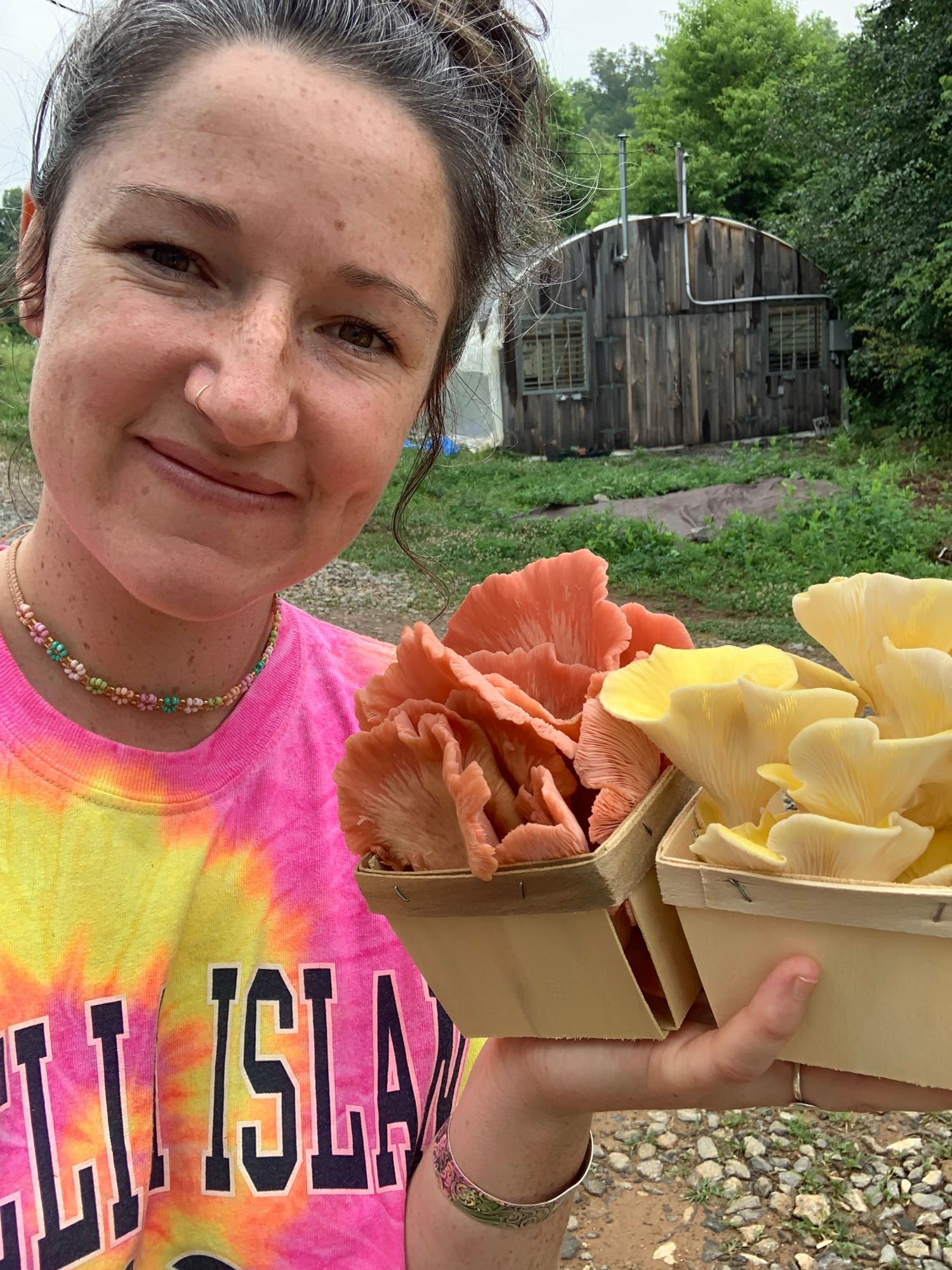 Taya holding baskets of pink and yellow oyster mushrooms, a fresh flush from her Mystic Roots grow