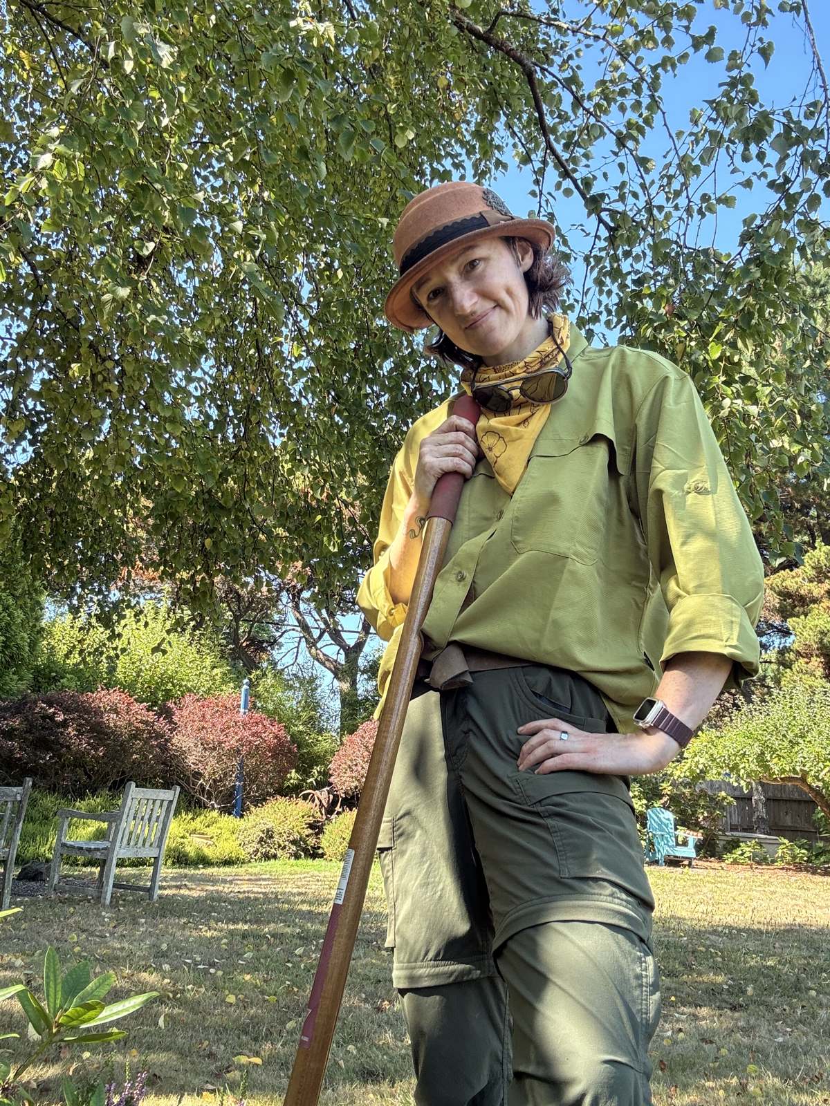 Taya, the Garden Faery, leaning on a garden tool under a birch in a Humboldt garden